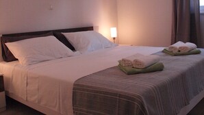 A neatly made bed with white linens, a headboard, and a painting above it.