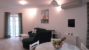 A compact living space with a dining table, a green sofa, a white chair, and a painting of a sailboat on the wall.