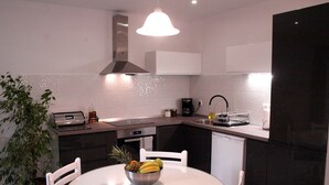A modern kitchen with a white table, chairs, a fruit bowl, a coffee maker, and a dishwasher.
