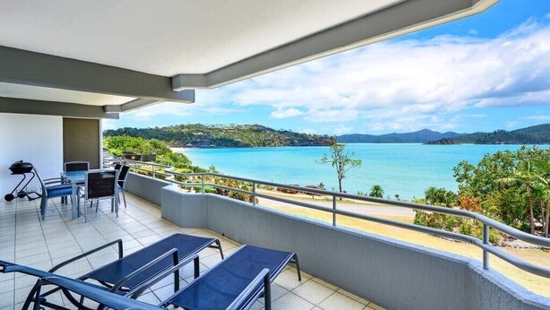 A balcony with a view of a beach and mountains. - Frangipani Lodge 008, Beachfront Apartment on Hamilton Island (Hamilton Island)