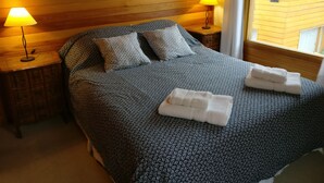 Una cama bien hecha con una colcha estampada y dos almohadas, flanqueada por mesitas de noche de madera con lámparas, en una habitación con paneles de madera y una ventana con vistas.