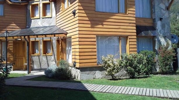 Una casa de madera de varios pisos con fachada de piedra, un porche cubierto y un césped cuidado.