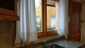 Una cocina con encimeras de granito, un lavamanos de acero inoxidable y una ventana con cortinas.