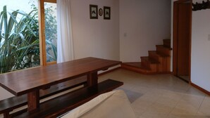 Una habitación con una mesa de madera, un banco, una escalera y vistas al verdor exterior.