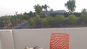 A round wooden table with a decorative metal tea set and a bright orange chair with a lattice backrest, set on a balcony with a view of trees and a road. - Colonels Home stay - A home away from home. Set in a scenic natural environment. (Sector 14)