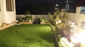 A nighttime view of a residential backyard with a well-maintained lawn, potted plants, and a streetlight. - Colonels Home stay - A home away from home. Set in a scenic natural environment. (Sector 14)