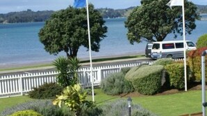 Vista al agua con valla blanca, una carretera y una camioneta blanca, y un árbol grande.