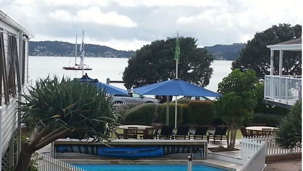 Zona de piscina con sillones de playa y sombrillas, con vistas a un lago y veleros.