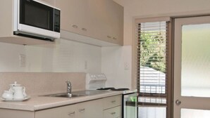 Una cocina moderna con microondas, estufa y lavamanos. Hay una ventana con persianas y una puerta con vidrio esmerilado.
