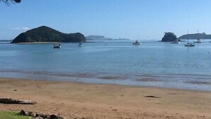 Una playa con agua tranquila, barcos y islas a lo lejos.