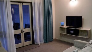 Una sala de estar con televisor sobre un mueble bajo, sofá y puerta corrediza de vidrio con cortinas.