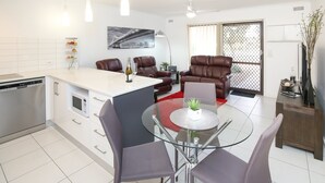 A modern kitchen with a dining area, featuring a glass table, leather chairs, and a view of a cityscape through a large window.