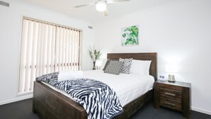 A neatly arranged bedroom with a wooden bed, a bedside table with a lamp, and a window with blinds. - Newly renovated 2 x Queen Bedrooms, weekly service, central location, free wifi (Mildura)