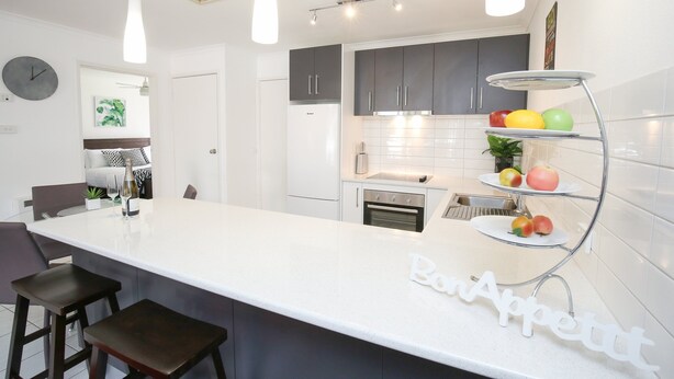 A modern kitchen with a white island, dark cabinets, and a fruit display.
