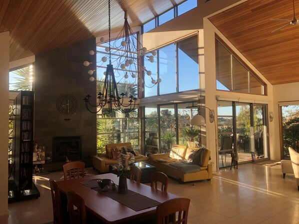 Un amplio salón con techo alto, ventanas grandes, chimenea y una mesa de comedor con sillas.