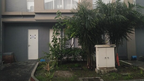 Un edificio moderno con tejado plano, ventanas amplias y un pequeño jardín con plantas y un armario de servicios.
