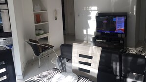 Un salon moderne doté d’un téléviseur à écran plat, d’un canapé, d’une table basse et d’un coin repas comprenant une chaise et une table.