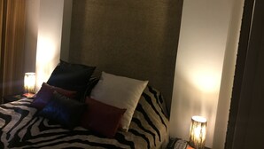Une chambre d’hôtel avec un grand lit, une literie à motifs zébrés et plusieurs oreillers. On y trouve deux lampes de chevet et un rideau sur le côté gauche.