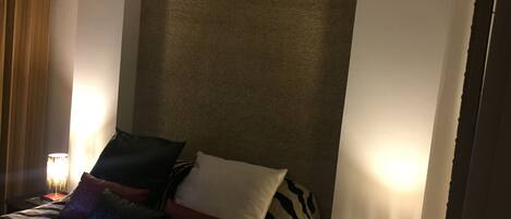 Et hotelværelse med en stor seng, sengetøj med zebra-mønster og flere puder. To sengeborde med lamper og et gardin på venstre side.