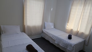 A small, clean room with two single beds, a bedside table with a lamp, and a window with curtains. - Apartment ground floor B (Willemstad)