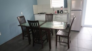 A compact kitchen with a dining table and four chairs, a microwave, and a refrigerator. - Apartment ground floor B (Willemstad)