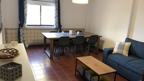 Een zithoek met een houten tafel en stoelen, een blauwe bank en een kleine tafel met opbergkisten.