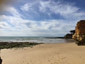 Une plage bordée d’une falaise rocheuse, sous un ciel dégagé.