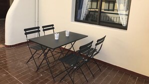 Een klein, afgesloten terras met een tafel en stoelen, een raam met gordijnen en uitzicht op een balkon.