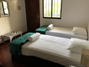 Une chambre avec deux lits simples, chacun recouvert d’une couette verte et agrémenté d’oreillers blancs. On y trouve également un banc en bois et une petite table dans un coin.