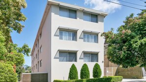 Un bâtiment moderne à deux étages, doté d’un toit plat, de fenêtres rectangulaires et d’une entrée fermée par un portail.