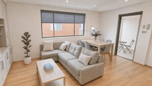 Un salon moderne avec un canapé beige, une table basse en bois et un coin repas comprenant une table et des chaises.