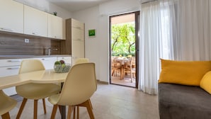 Eine moderne Küche mit weißen Schränken, ein Essbereich mit Tisch und Stühlen sowie ein Sofa mit gelbem Kissen.