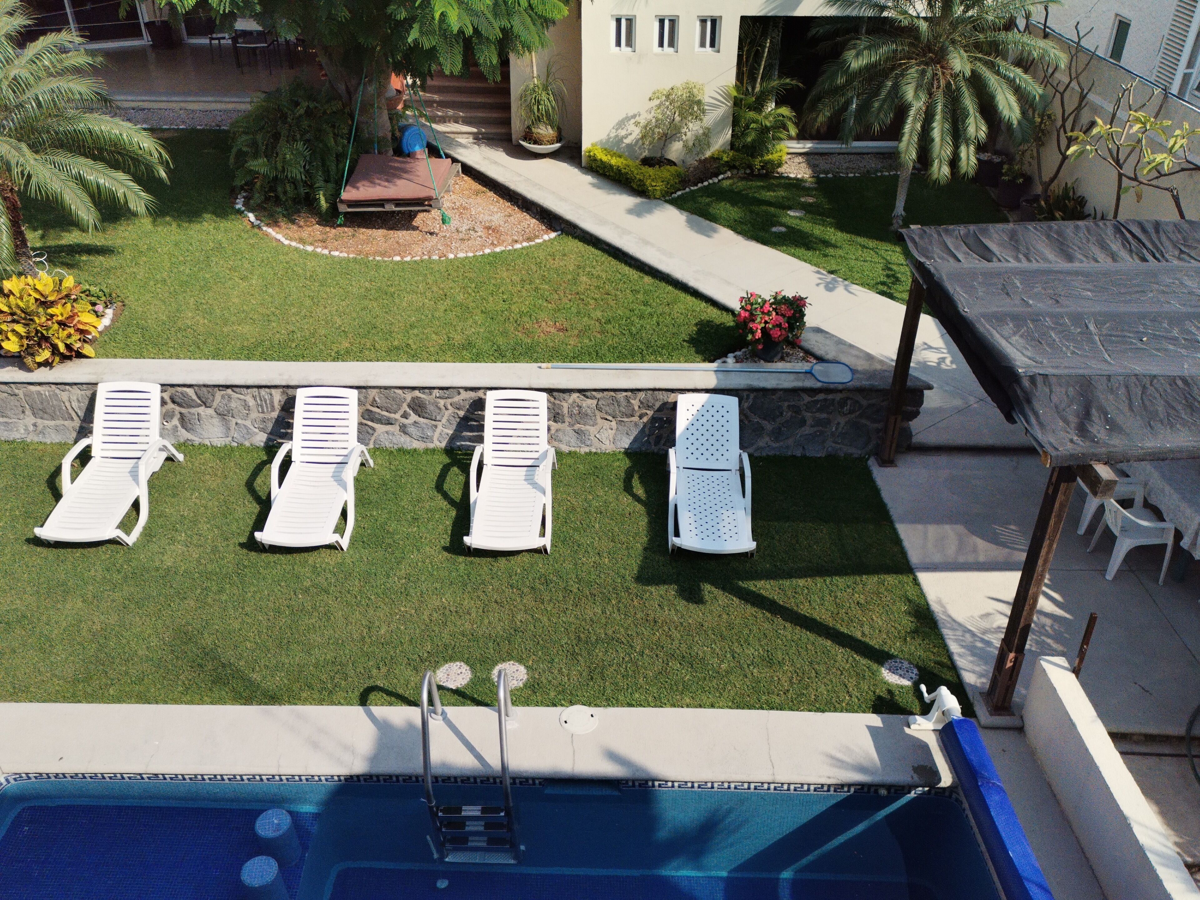 Un espace piscine comprenant quatre chaises longues blanches, une petite piscine avec une échelle et un mur en pierre.