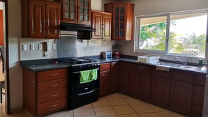 A kitchen with wooden cabinets, a stove, and a window with a view of greenery.