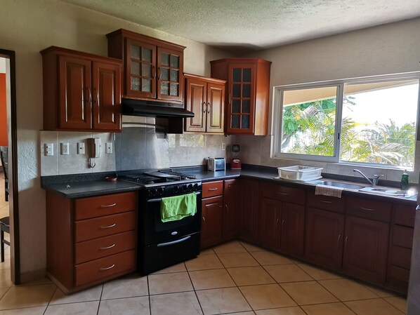 A kitchen with wooden cabinets, a stove, and a window with a view of greenery. - Ideal para descansar y divertirse con la familia o con amigos. (Burgos Bugambilias)