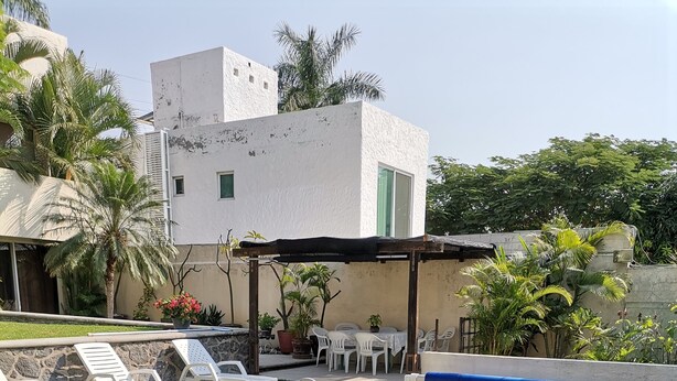 A swimming pool with a tiled edge, surrounded by a grassy area and white lounge chairs.