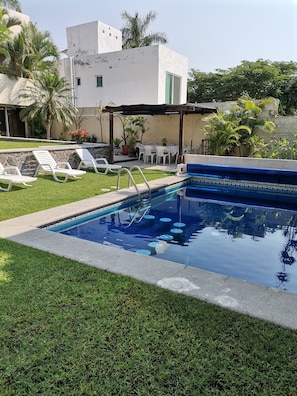 A swimming pool with a tiled edge, surrounded by a grassy area and white lounge chairs.
