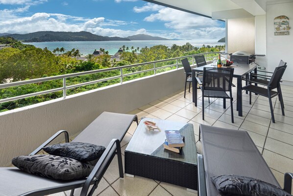 Un balcon avec vue sur la mer, un coin repas avec des chaises et une table, et un barbecue.