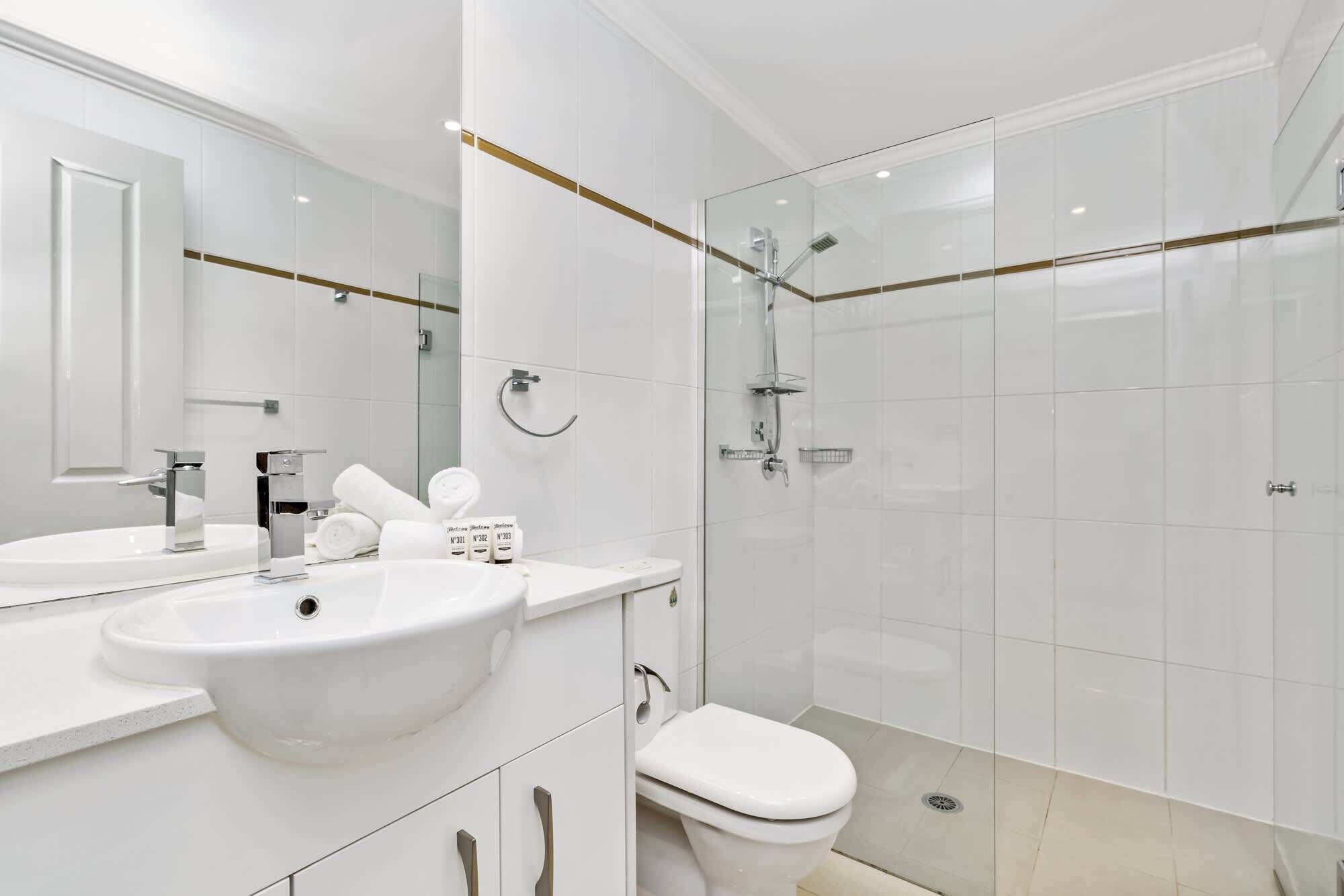 A modern bathroom with a large mirror, a white sink, a toilet, and a glass-enclosed shower area.