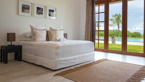 A bedroom with a large bed, a nightstand, a lamp, and a view of a pool through the glass doors.