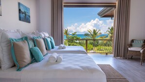 A hotel room with two beds, a balcony with a view of the ocean, and a wicker chair.