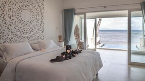Un dormitorio con una cama grande, un adorno en la pared y vista al mar a través de un ventanal corredera.