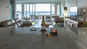 Una sala de estar moderna con vista al océano, una mesa de comedor con una botella de vino y copas, y una zona de estar acogedora.