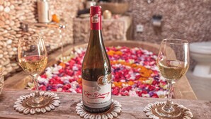 Una botella de vino y dos copas sobre una mesa de madera con un lecho de pétalos de flores.