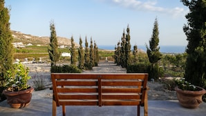 Un banc dans un jardin, avec des plantes en pot de chaque côté, qui offre une vue sur la mer et les bâtiments situés au loin.