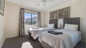 Habitación de hotel con dos camas, ventilador de techo, ventana grande con cortinas y vistas al exterior.