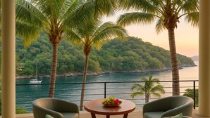 A balcony with two chairs and a table, overlooking a body of water with a sailboat and a forested island. - Experience Luxury Living at Our Ocean Front Villa in Puerto Vallarta
 (Amapas - Conchas Chinas)