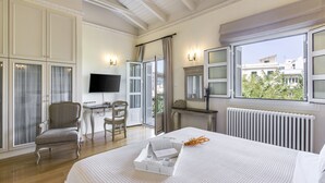 A hotel room with a bed, a desk, a chair, a TV, and a view of buildings outside. - Aerides 3 Luxury Suites - the heart of the historic center, with Acropolis view (Athens)