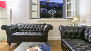 A room with a black leather sofa, a marble coffee table, and a window with a view of a building on a hill. - Aerides 3 Luxury Suites - the heart of the historic center, with Acropolis view (Athens)