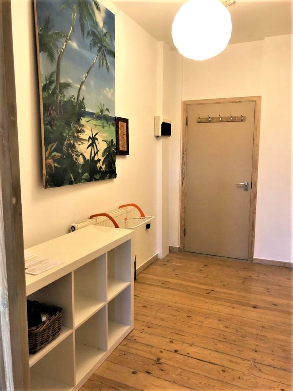 Ein Korridor mit Holzboden, einer weißen Bank mit Ablagen, einer Tür mit Griff und einer wandmontierten Leuchte.